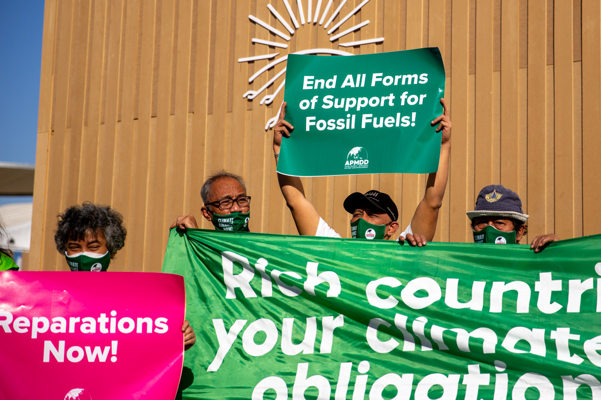 Eine Person auf der COP27 hält ein Schild in die Luft, auf dem staht "End All Forms of Support for Fossil Fuels!"