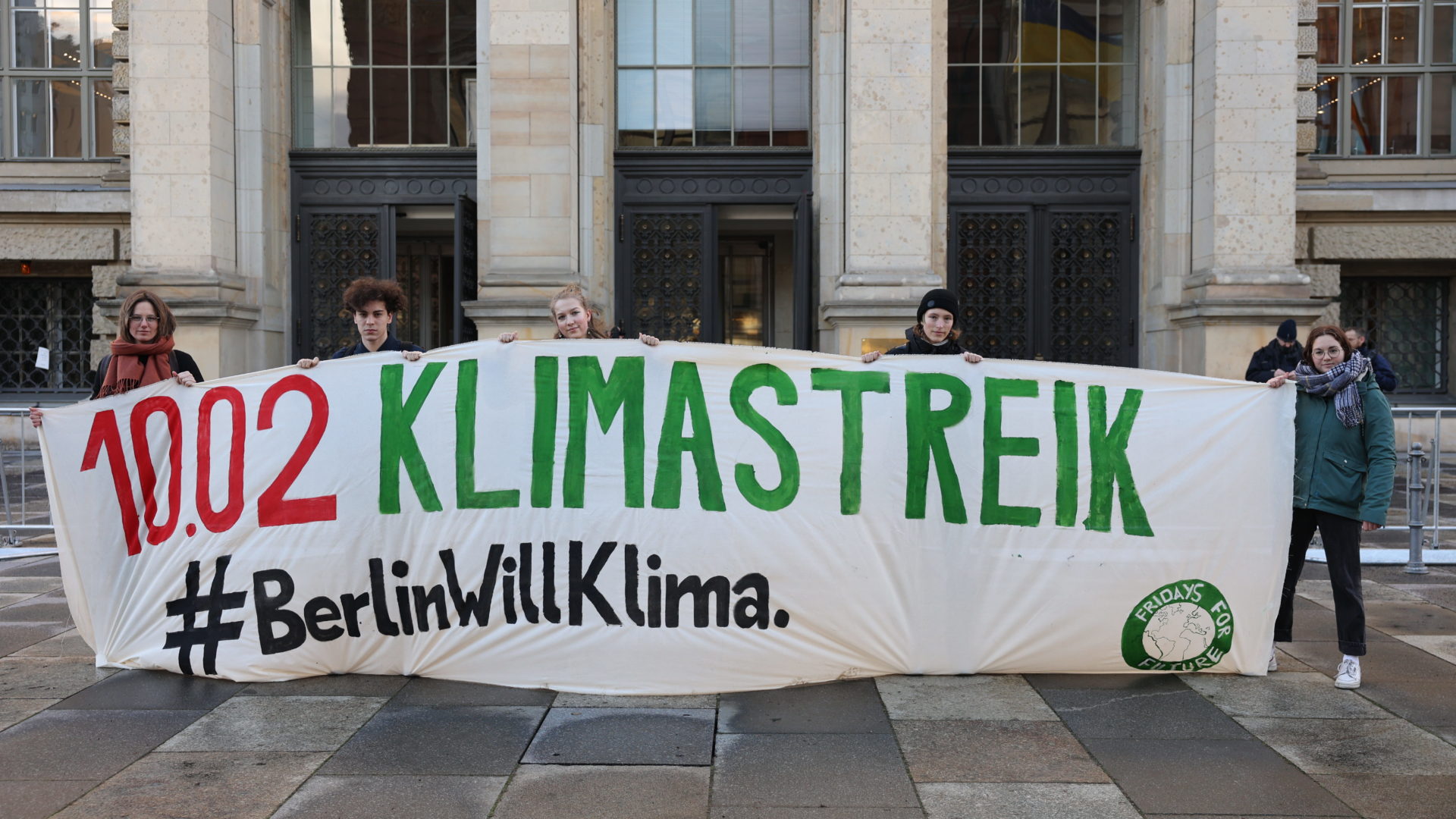 Klimaaktivist*innen halten ein Banner mit der Aufschrift "10.2. Klimastreik #BerlinWillKlima". Sie stehen vor dem Berliner Abgeordnetenhaus.