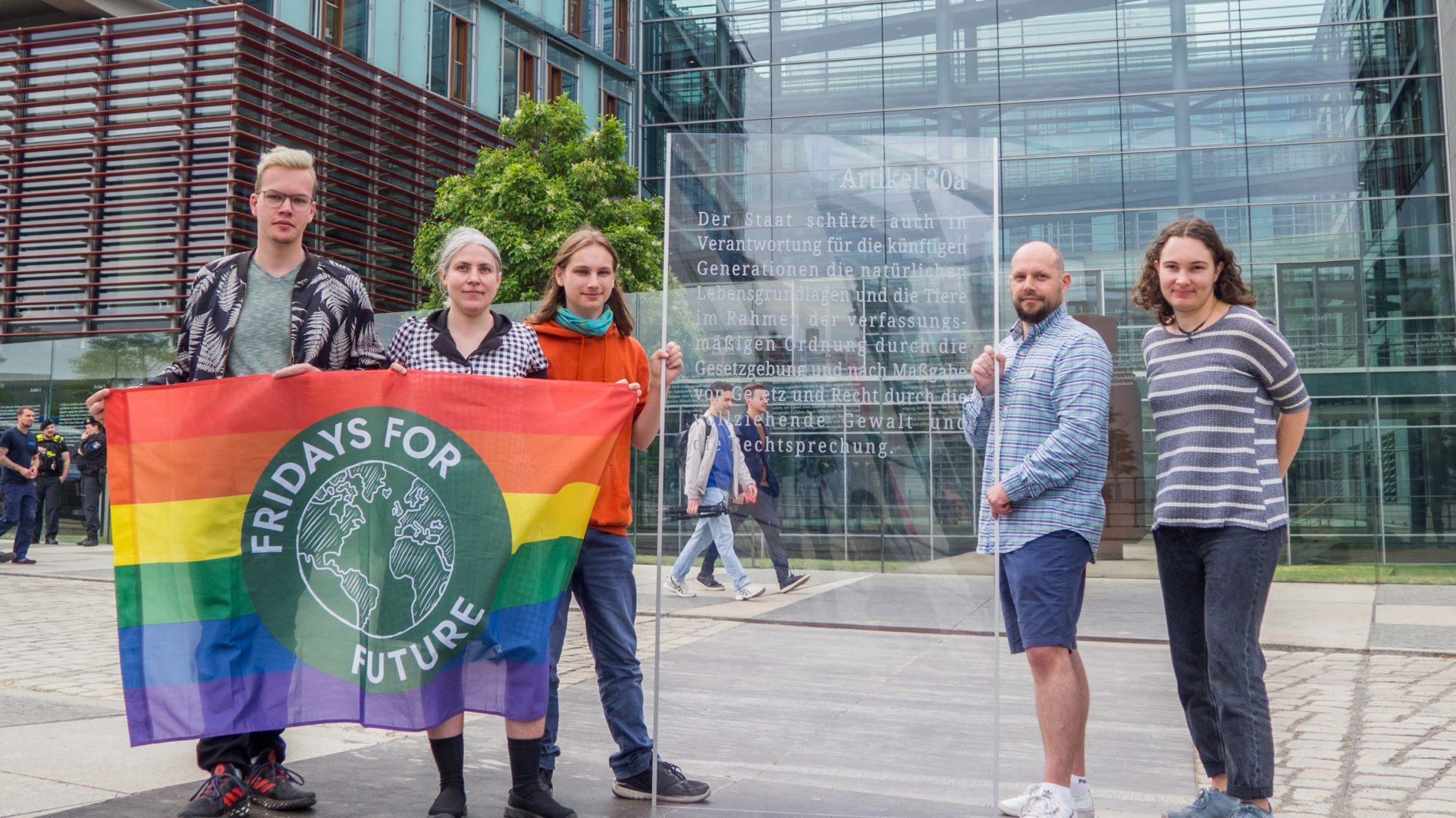 Aktivist*innen stehen mit einer FFF Fahne vor dem Grundgesetzdenkmal am Bundestag, sie präsentieren eine Glasscheibe im Stil des Denkmals auf die der Artikel 20a graviert wurde